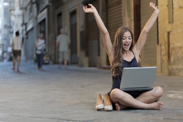 Sediaca žena s laptopom, ulica, ruky hore