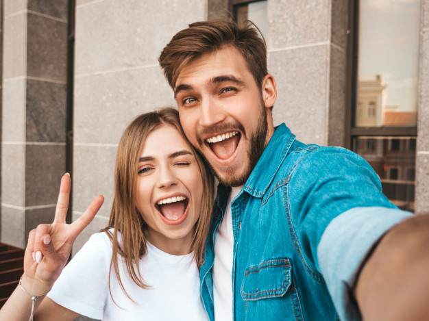 smiling-beautiful-girl-her-handsome-boyfriend-casual-summer-clothes-happy-family-taking-selfie-self-portrait-themselves-smartphone-camera-shows-peace-sign-winking-street_158538-5459